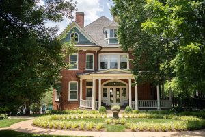Hospice of the Piedmont's Hospice House in Charlottesville Virginia is a classic red brick Victorian with a wrap around front porch, it sits in level landscaped yard with mature leafy trees.