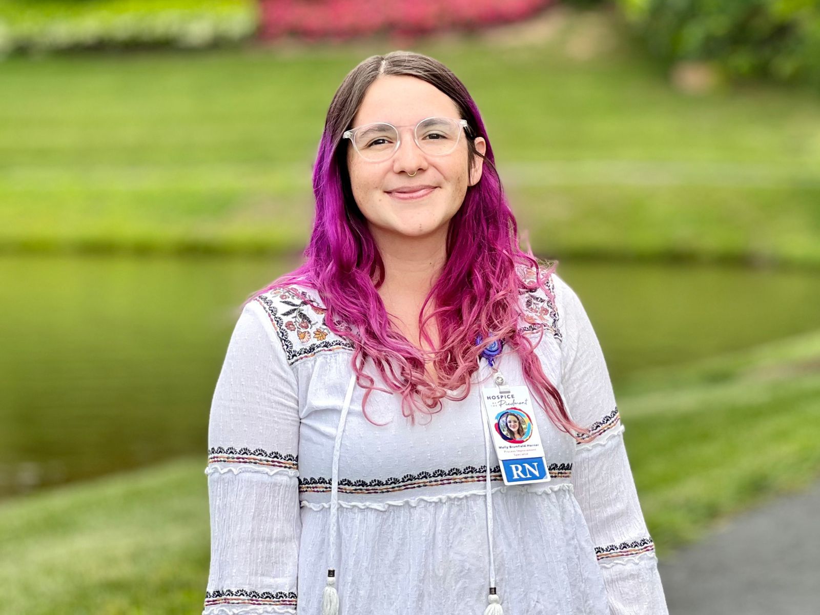 Molly Brumfield Horner smiling and standing in front of a pond with grass and a sidewalk.