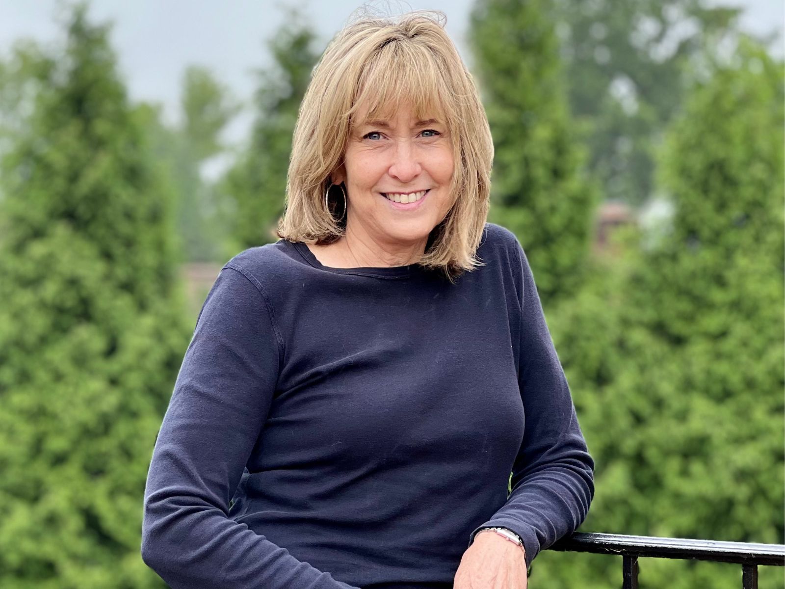 Robin Johnson smiling leaning on a railing in front of a blurry tree background