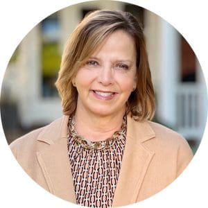 Nancy Littlefield, Hospice of the Piedmont CEO, wears a tan blazer and patterned shirt standing in front of the Hospice House