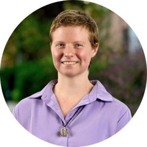 Dr. Kellie Mitchell wears a light purple shirt and stands in front of some plants