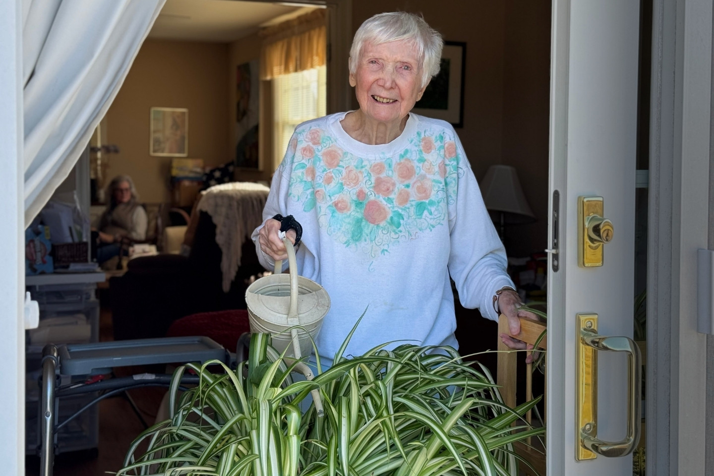 A Palliative Medicine patient in a shite sweatshirt with hand painted along the top waters plants on a balcony