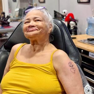 A hospice patient in a yellow tank top shows off her new tattoo: a line drawing of a heart with a flower growing out of it