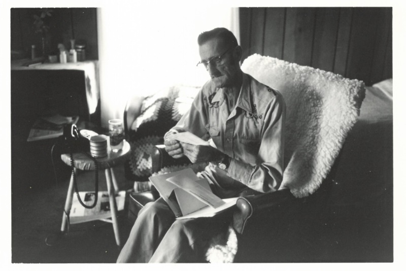 Black and whit photo of Man in Cowboy Shirt Looks at Mail in Recliner