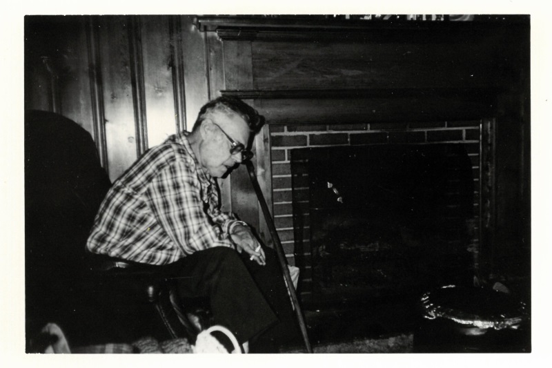 Black and white photo of Man with Cane Smokes Next to Fireplace