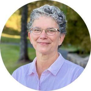 Beth Epstein wears metal framed glasses and a pink striped button down shirt